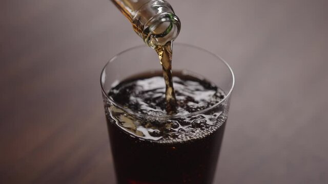 Slow motion man pour cola into tumbler glass on walnut table with copy space