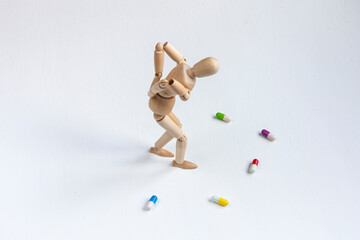 a bent wooden mannequin with back pain among colorful pills on white background