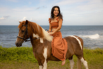 Happy smiling woman riding horse near the ocean. Outdoor activities. Traveling concept. Bali