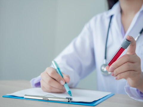 skillfull doctor in gown and stethoscope holding  blood tube and taking note on patient chart at a hospital or clinic. lap worker or professional concept.
