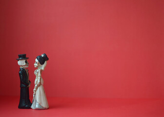 A close-up shot of two skeletons standing in profile. Photo for Day of the Dead, Halloween or Valentine's Day on a bright red background. Copy space