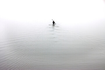 Fototapeta premium High key image of a silhouette of a man rowing a canoe. Minimalist photography concept