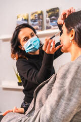 A makeup artist with a face mask with the concealer brush. Security measures of aesthetic centers in the Covid-19 pandemic