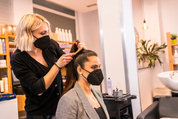 Hairdresser with mask finishing the hairstyle to the brunette client. Security measures of Hairdressers in the Covid-19 pandemic
