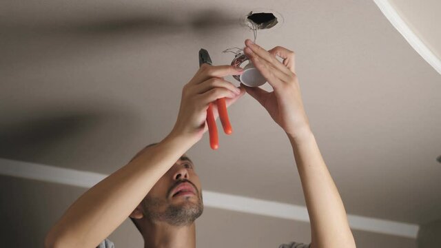 A man uses pliers while repairing a ceiling LED light fixture