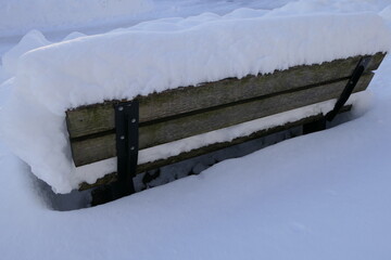 Beautiful frosty scene with thickly snowed wooden bench in the deep winter