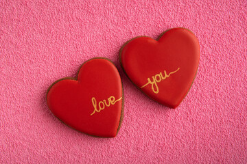 Two red cookies in shape of hearts with the inscription LOVE YOU on pink background.
