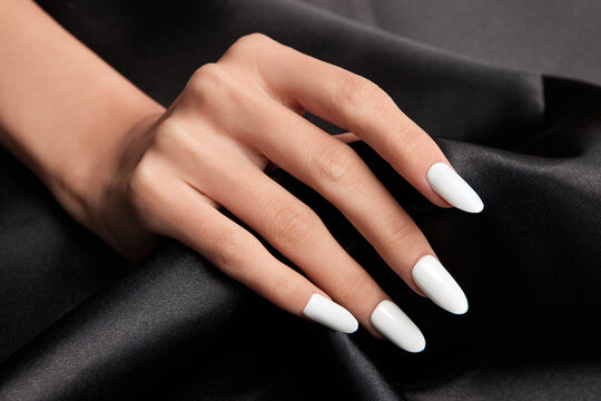 Female hand with long white nails holding a black satin fabric