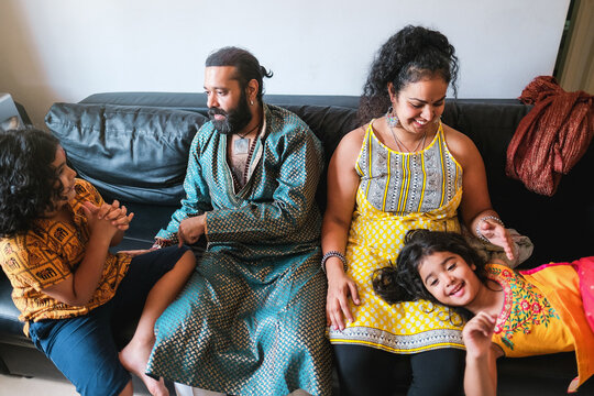 Happy indian family playing together at home sitting on sofa - Focus on woman