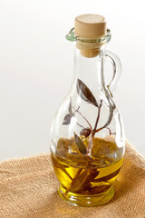 Olive oil and a sprig of olive in a glass jug standing on a burlap sack. White background. Space for your text. Close up.