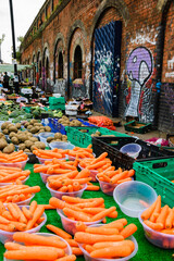 Fresh sweet carrots, potatoes, broccoli at Brick Lane market. Old building with graffities at backgrounds.