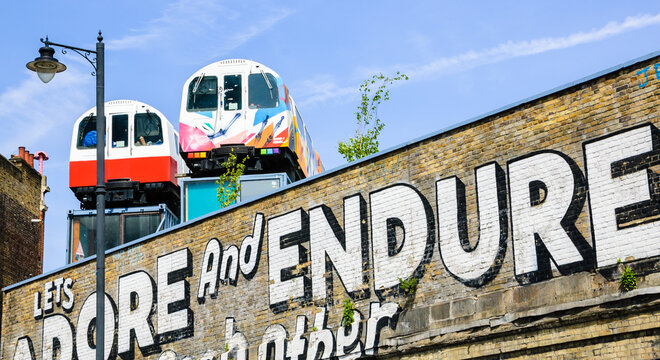 London, England, UK - May 4, 2014: Graffiti on the Village Underground wall and old colorful train wagons behind it in Brick Lane area. Urban art in this area attracts tourists from all over the world