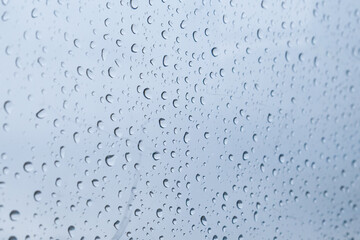 Rain drops on the scratches glass background. Blue cloudy sky behind. Selective focus. Diagonal.