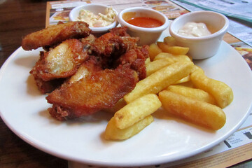 Roasted chicken with french fries and sauce on a plate. Wooden background. Close up
