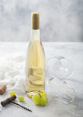 Empty glasses and bottle of summer white wine with grapes, corks and corkscrew on light background.