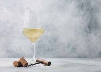 Glass of summer white wine with corks and corkscrew on light background.