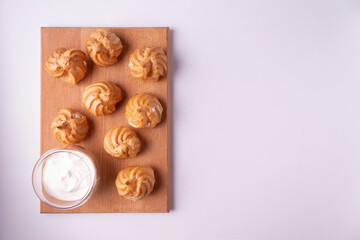 Choux pastry profiteroles on a wooden board on a white background. Flat lay.