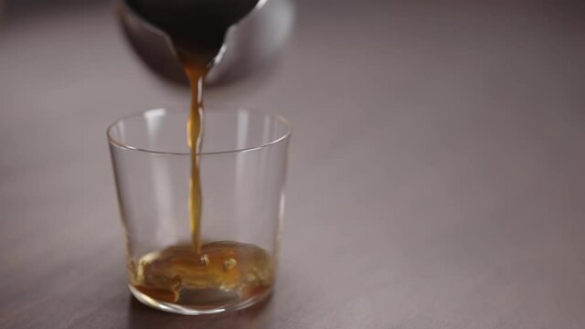 Slow motion coffee pour into tumbler glass on walnut table