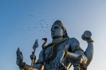 Landscape view of the second tallest Lord Shiva statue in the world with a flock of flying birds in Murdeshwar, Karnataka, India