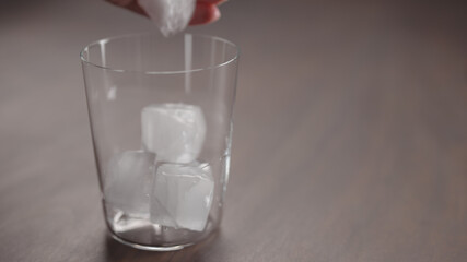 man add ice cubes into tumbler glass on walnut table with copy space