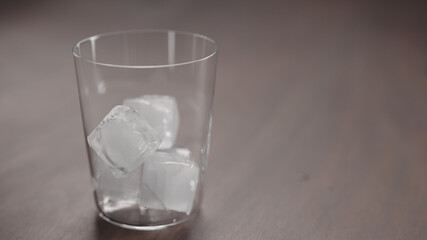 ice cubes into tumbler glass on walnut table with copy space