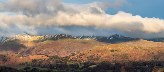 Majestic Winter landscape image view from Holme Fell in Lake District towards snow capped mountain ranges in distance in glorious evening light with Autumnal colors trees