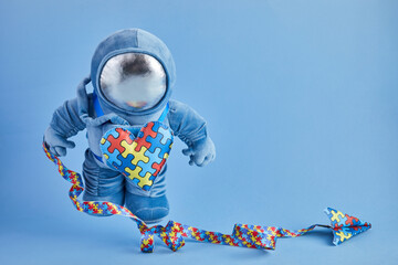 Autism awareness background. Blue plush astronaut toy with puzzle heart, autism symbol, on blue background