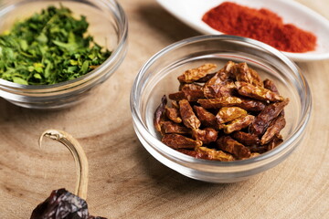 Chilli pepper in glass bowl on wooden log with other spices