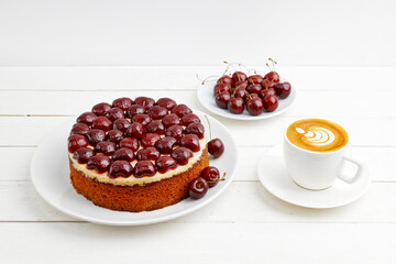 Homemade cake with cherries and cup of coffee cappuccino on white wooden table. Shallow focus.