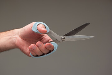 Caucasian male hand holding a special scissors made for left-handed people isolated on gray background