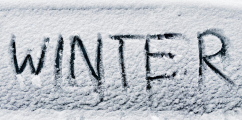 word winter written with finger in frsh snow on car window
