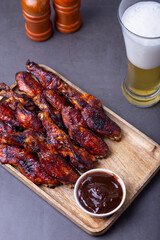Fried chicken wings on a wooden board with barbecue sauce and a glass of beer. Black background, close-up.