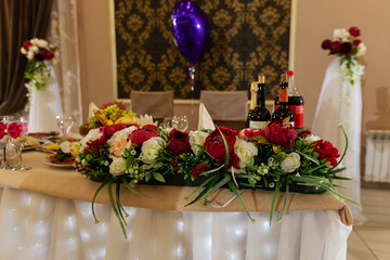 decorations with flowers at the wedding, the interior of the restaurant is prepared by the decorator for the holiday, beautiful fresh flowers in vases on the table, a bouquet as a gift from the guests