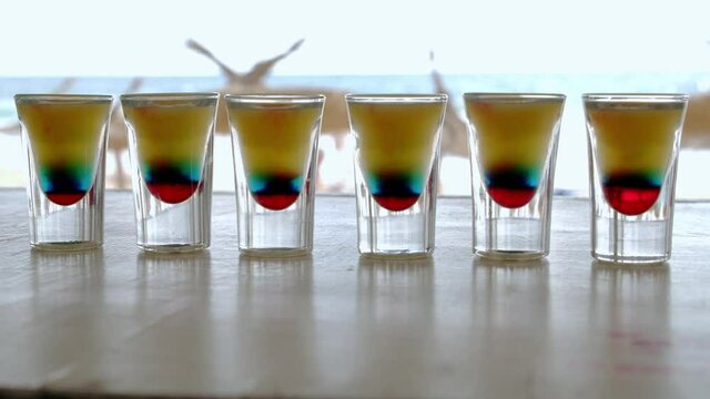 Glasses with colorful shots lined up on the beach bar on a hot summer day, 4k slow motion