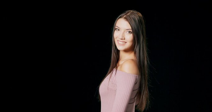 A long-haired brunette model turns toward the camera and smiles against a black studio background with copy space.