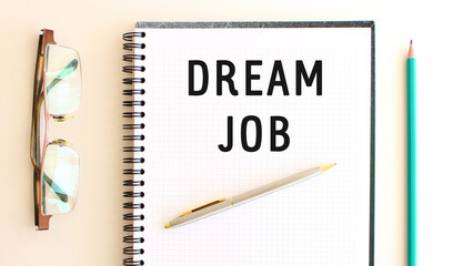 Notepad with text DREAM JOB on a white background, near glasses and pencil.