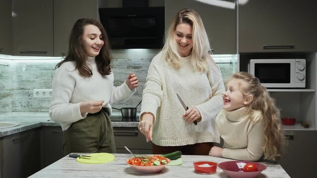 Young mother and two her daughters cooks salad at kitchen. Mother salt salad. Salt bae