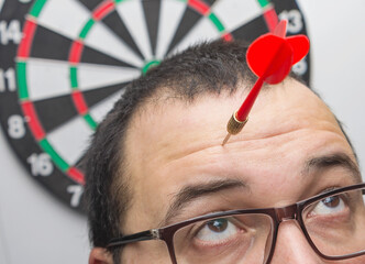 A dart in the forehead of a surprised man. Accident insurance, head shot, concept image