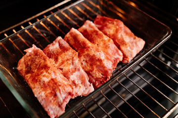 raw pork ribs sprinkle with salt, black pepper and paprika in a glass baking tray in the oven. cooking meat at home. Cook.