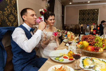 the newlyweds hold beautiful crystal glasses in their hands, the tradition of drinking alcohol at a wedding, a toast in a restaurant from the bride and groom
