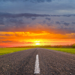 asphalt road among green fields at the sunset