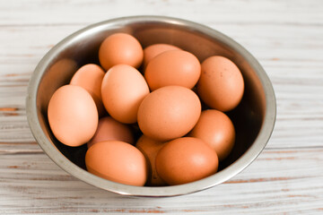 Fresh chicken eggs in a metal bowl on a light wood background. Village. Organic farm product concept.