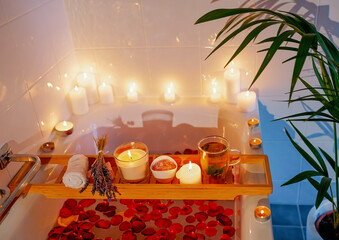Bath tray with herbal mint tea, candles, lavender and pink rose salt during spiritual aura cleansing rose flower bath with petals for full moon ritual. Body care and mental health routine.