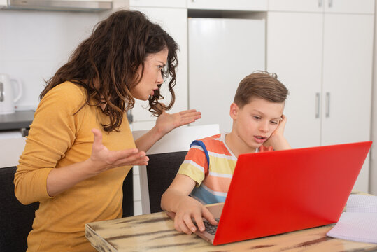 Upset mother looking in face of her son being silly while doing online class