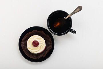 Cake basket with cream and raspberries, on a black saucer with a cup of tea. on a light background