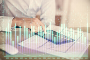 Double exposure of man's hands holding and using a digital device and forex graph drawing. Financial market concept.