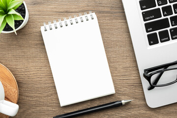 Blank notebook with pen are on top of wood office desk table with laptop computer, cup of coffee and supplies. Top view, flat lay.