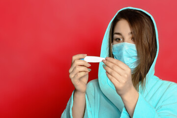 young woman in a mask on a red background holding a thermometer