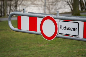 Sign before a green meadow saying: Flood ( germann: Hochwasser). The River Neckar is in the...