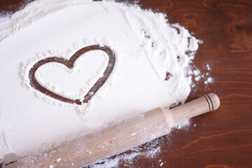 Fototapeta na wymiar heart on flour and a wooden rolling pin